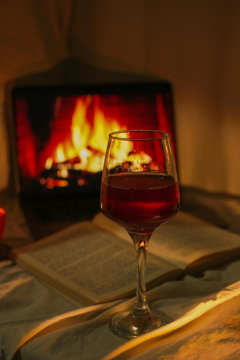 Glass of Red Wine against Open Book and Fireplace Image on Laptop